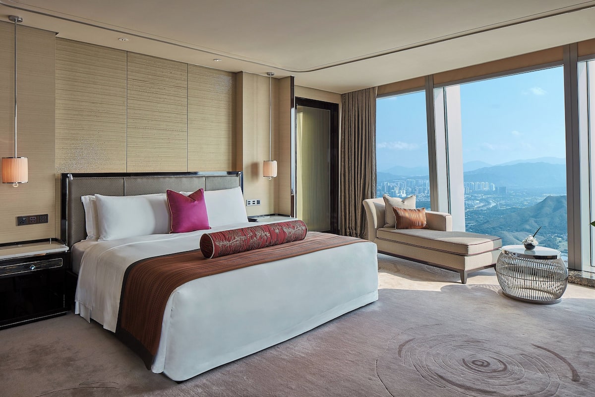 A modern hotel room with a large bed, a sofa, and a view of the city.
