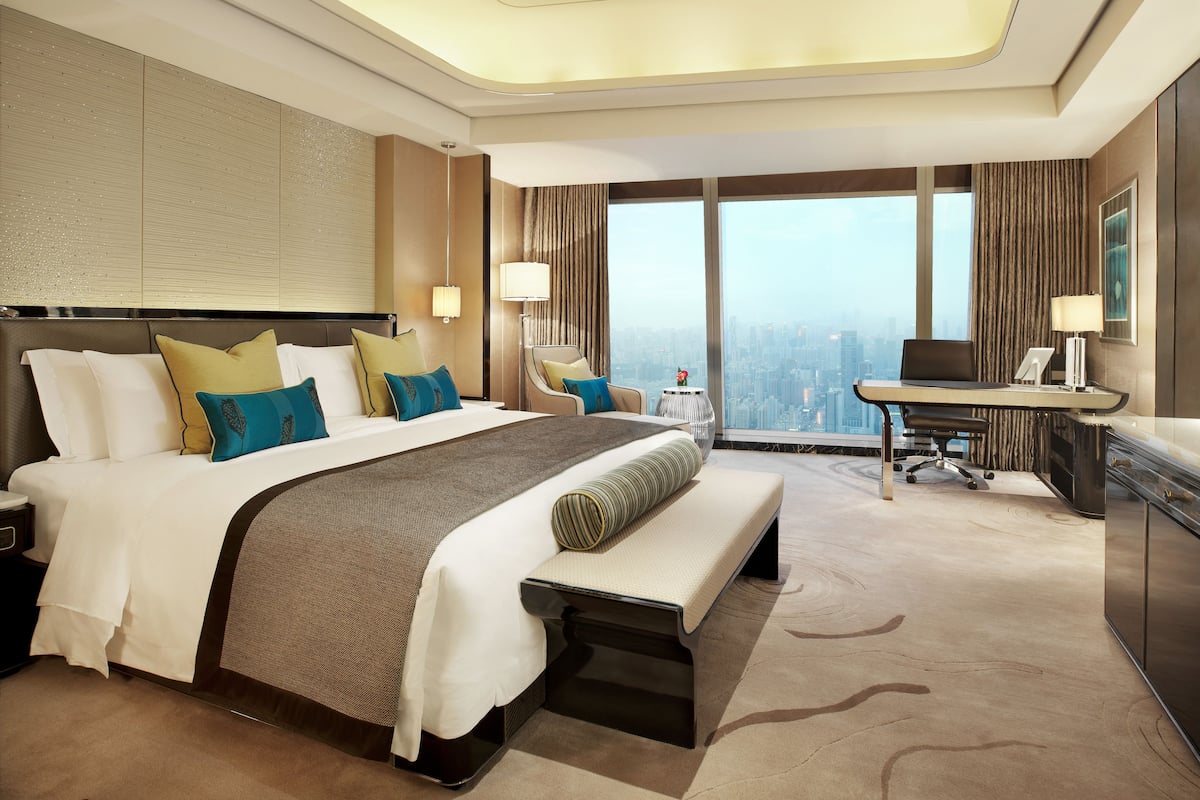 A modern hotel room with a large bed, a desk, and a view of the city.
