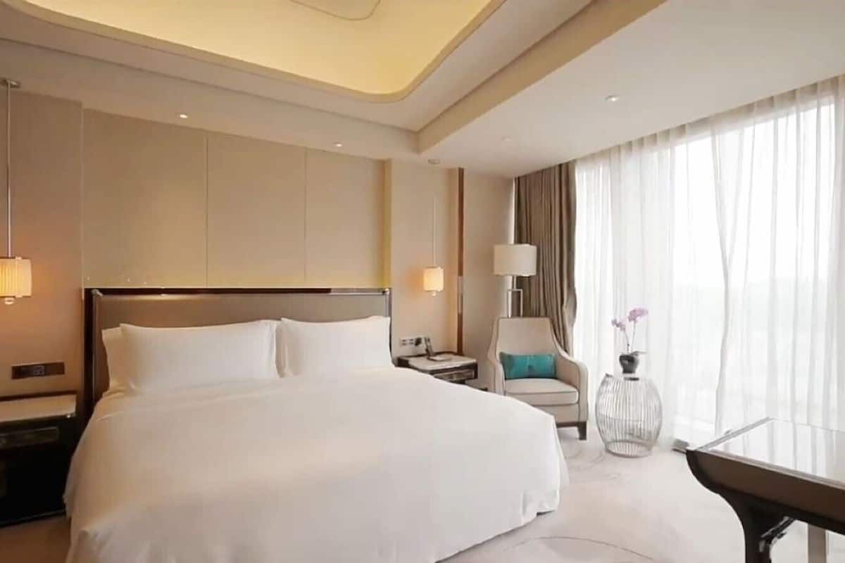 A hotel room with a large bed, bedside tables, a chair, a desk, and a window with curtains.
