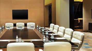 A conference room with a large table, multiple chairs, and a flat-screen TV on the wall.