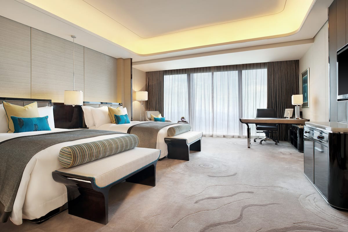 A modern hotel room with two beds, a desk, and a television.