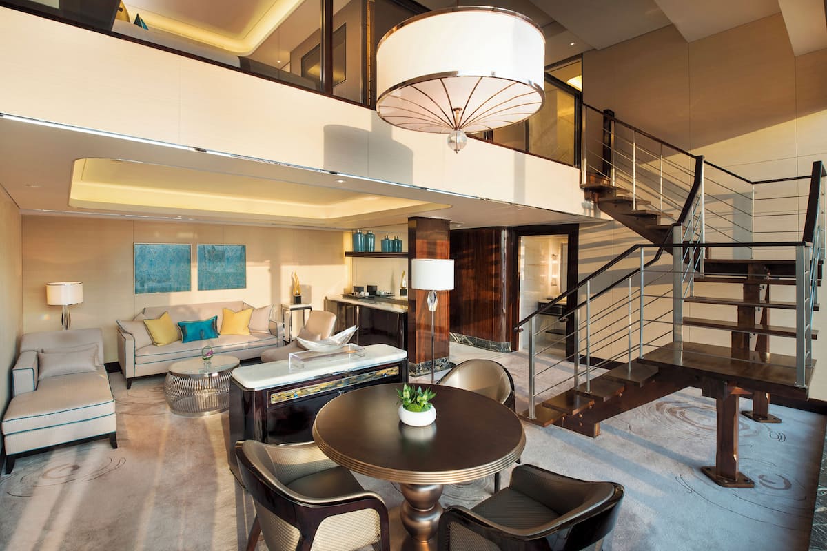 A spacious living area with a sofa, coffee table, and chairs, a staircase, and a dining area with a table and chairs.