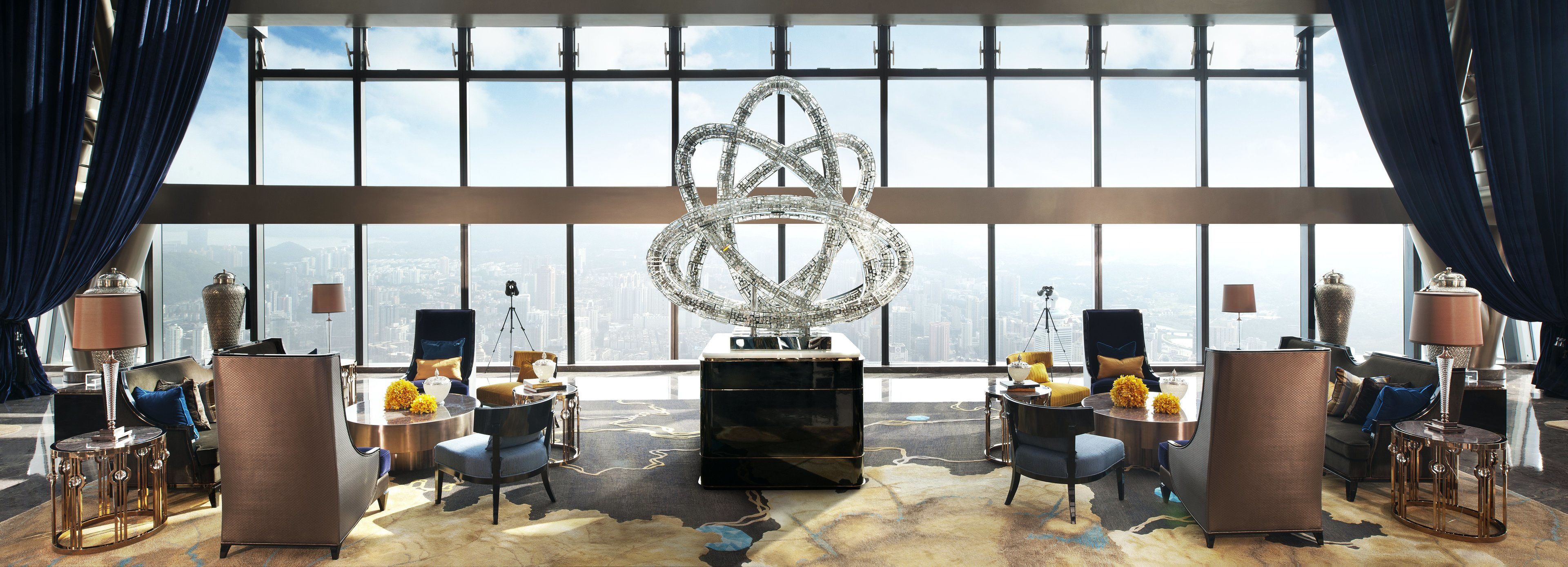A high-rise hotel room with a large city view, a modern chandelier, and contemporary furnishings.