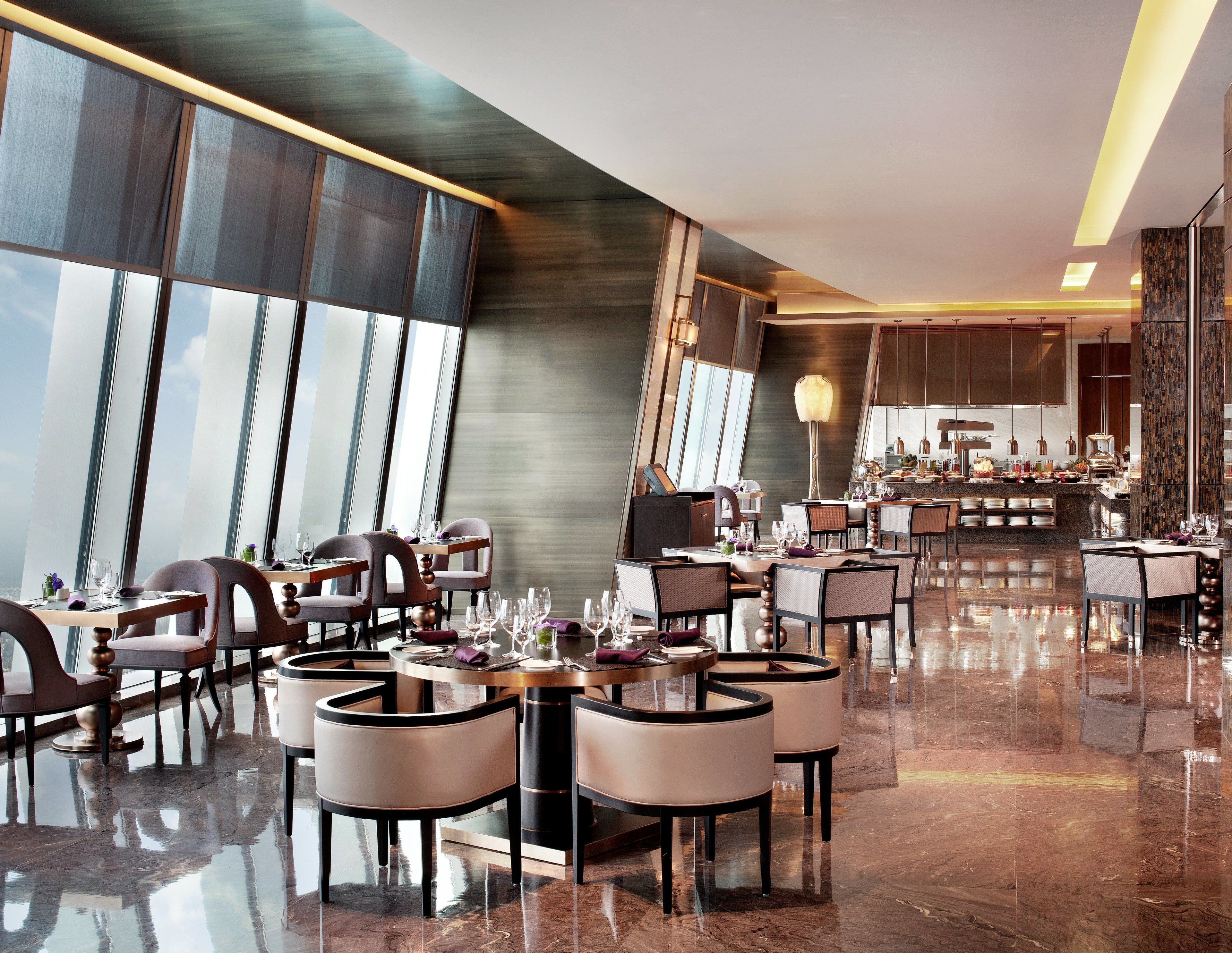 A modern restaurant with high ceilings, large windows, and a polished marble floor.