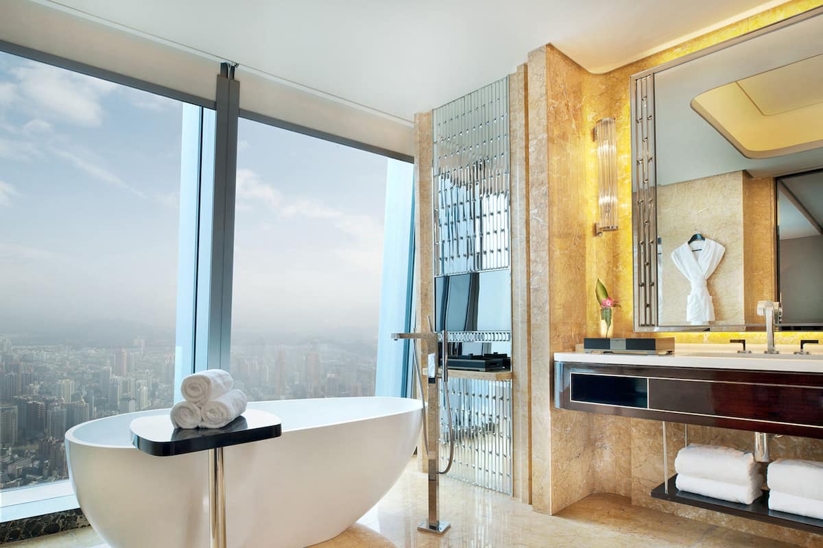 A modern bathroom with a freestanding bathtub, a large mirror, and a city view.