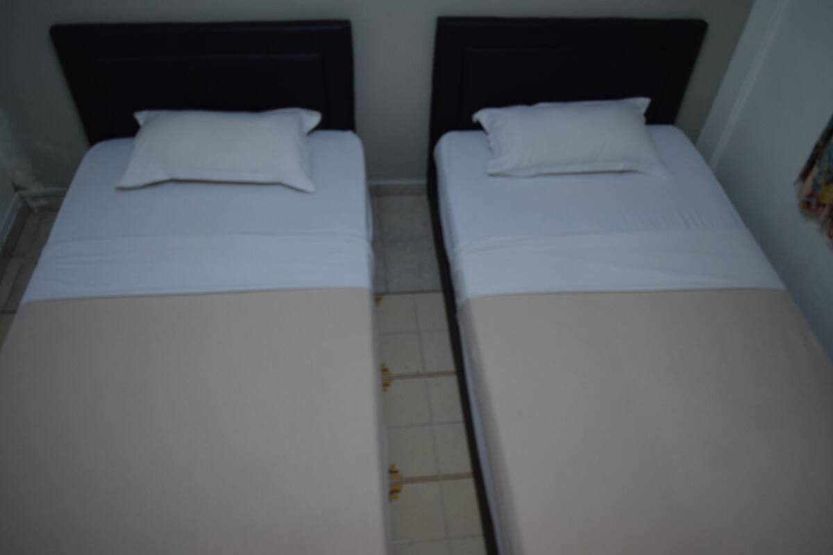 Two single beds with white linens and dark headboards in a room with tiled flooring.