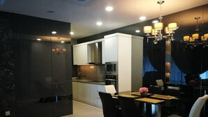 A modern kitchen with white cabinets, a dining area with a wooden table and black chairs, and a chandelier with multiple light fixtures. - Casa Blanca Guest House (Malacca City)