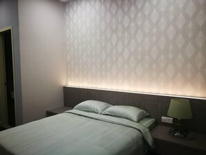 Una cama bien hecha con edredón y almohadas de color claro, una mesita de noche con lámpara y un papel tapiz estampado en la pared.