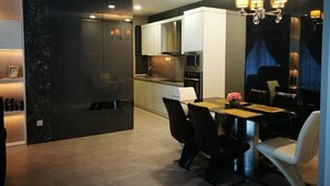 A modern kitchen with dark cabinetry, a dining area with a table and chairs, and a chandelier. - Casa Blanca Guest House (Malacca City)