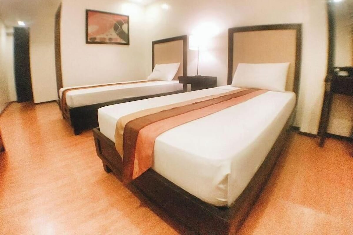 Quarto de hotel com duas camas, uma mesa de cabeceira, um abajur e um quadro na parede.