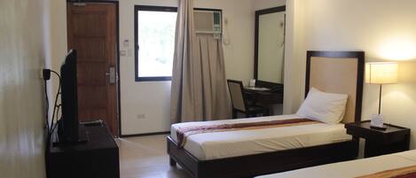 A hotel room with two beds, a desk, a chair, a TV, and a lamp.