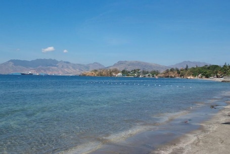 A coastal scene with clear water, a sandy beach, and mountains in the background.