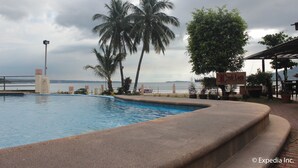A swimming pool with palm trees and a view of the ocean. - Subic Grand Seas Resort (Olongapo)