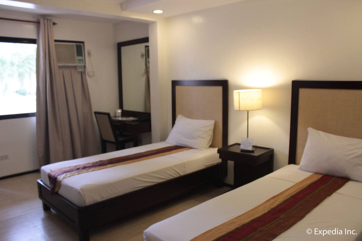 Quarto de hotel com duas camas, uma escrivaninha e uma cadeira.