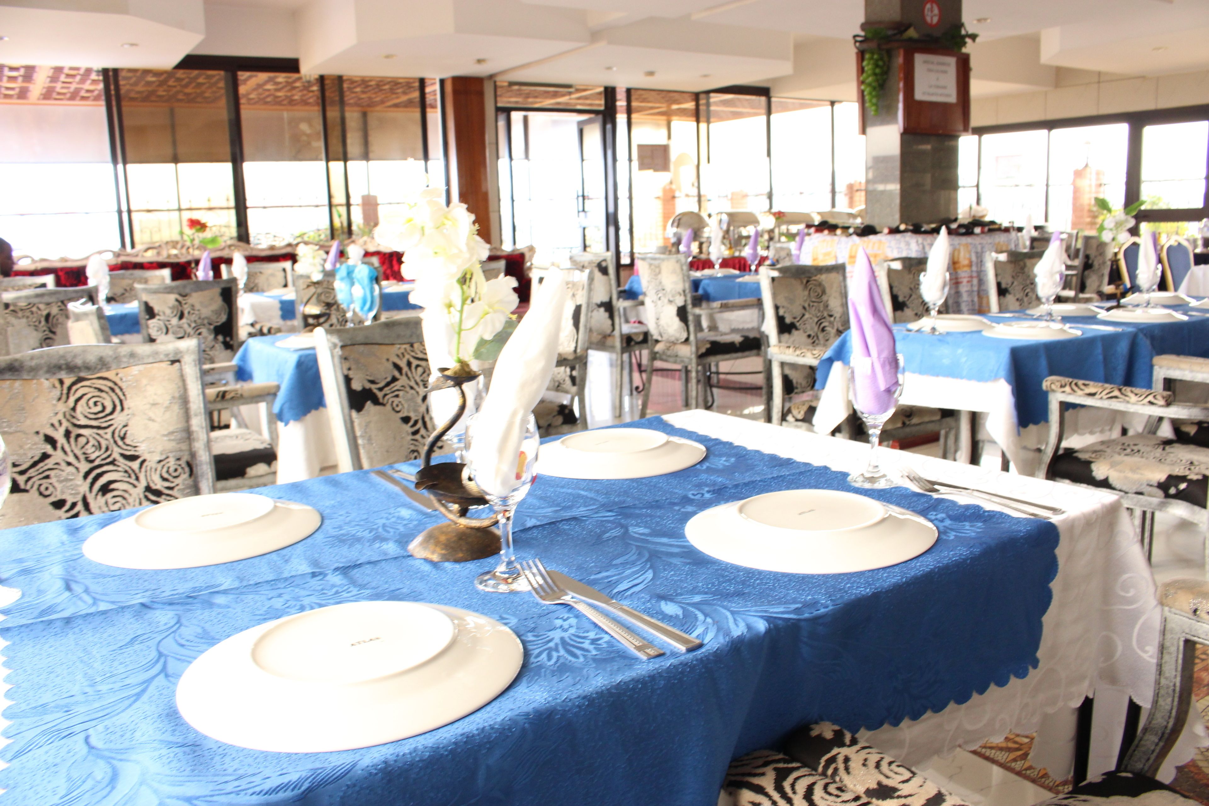 Un espace repas avec des tables dressées pour quatre personnes, chacune agrémentée d’assiettes blanches, de couverts et de nappes bleues.
