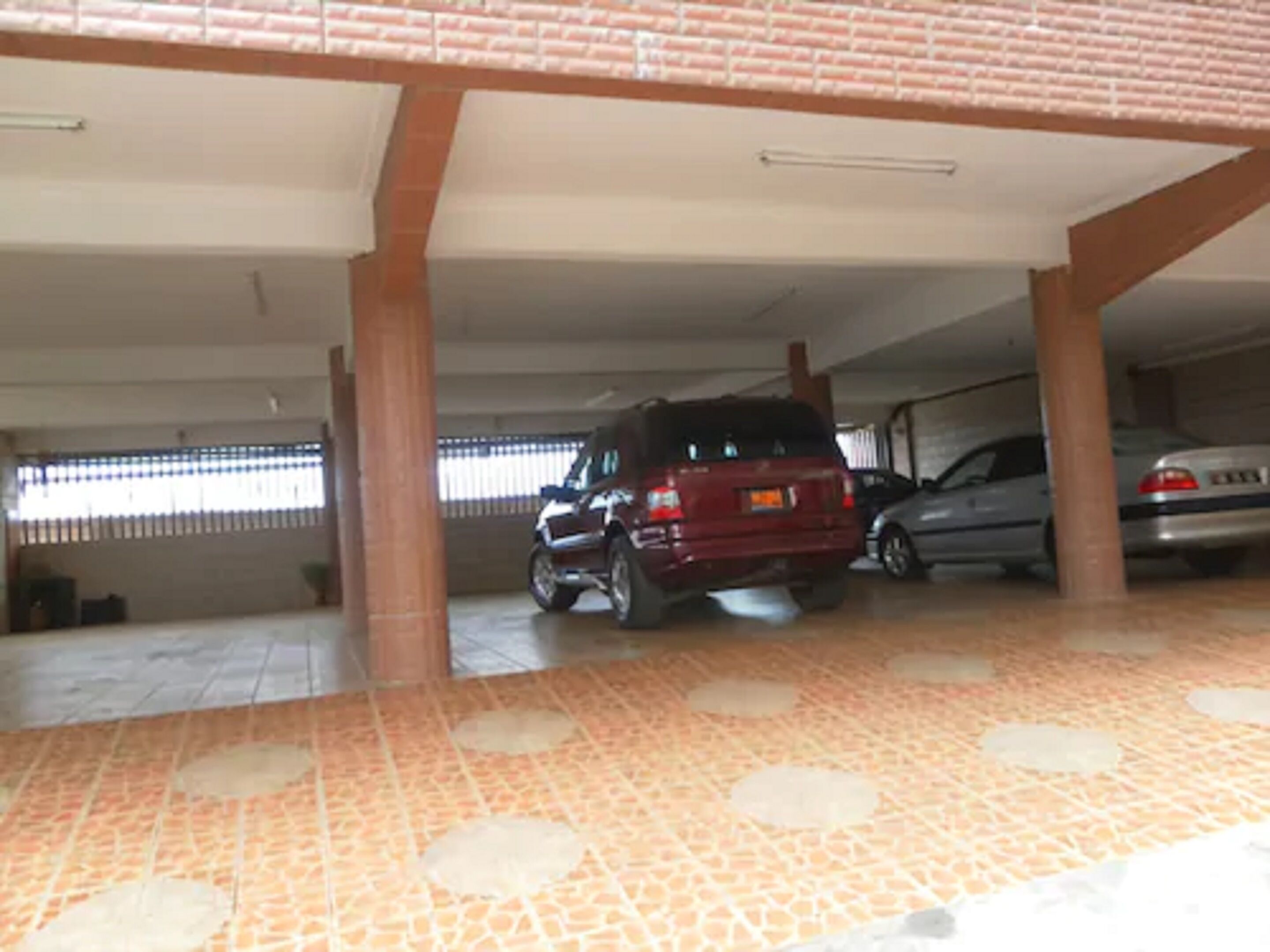A covered parking area with tiled flooring and a red vehicle parked in the foreground.