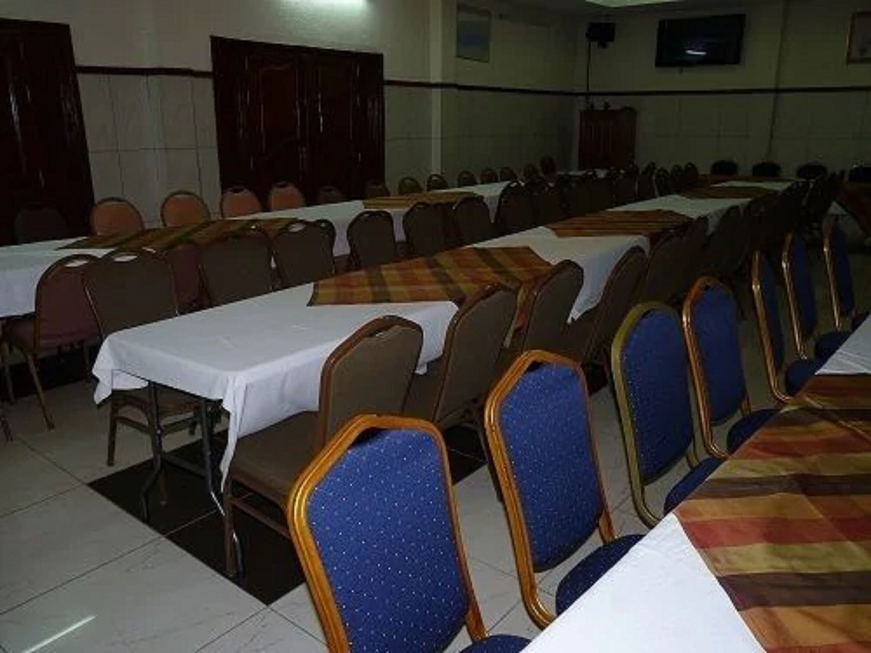 A conference room with rows of tables and chairs, a television screen, and a tiled floor.