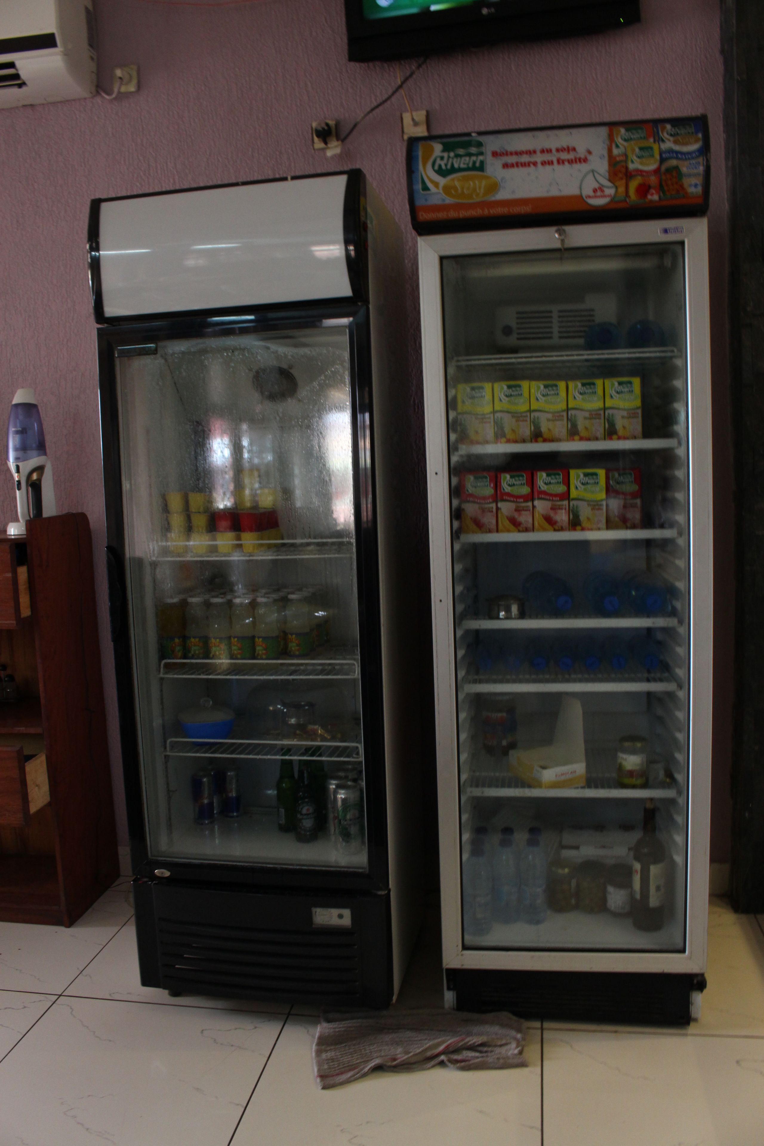 Two beverage vending machines with various drink options, located in a room with a tiled floor.