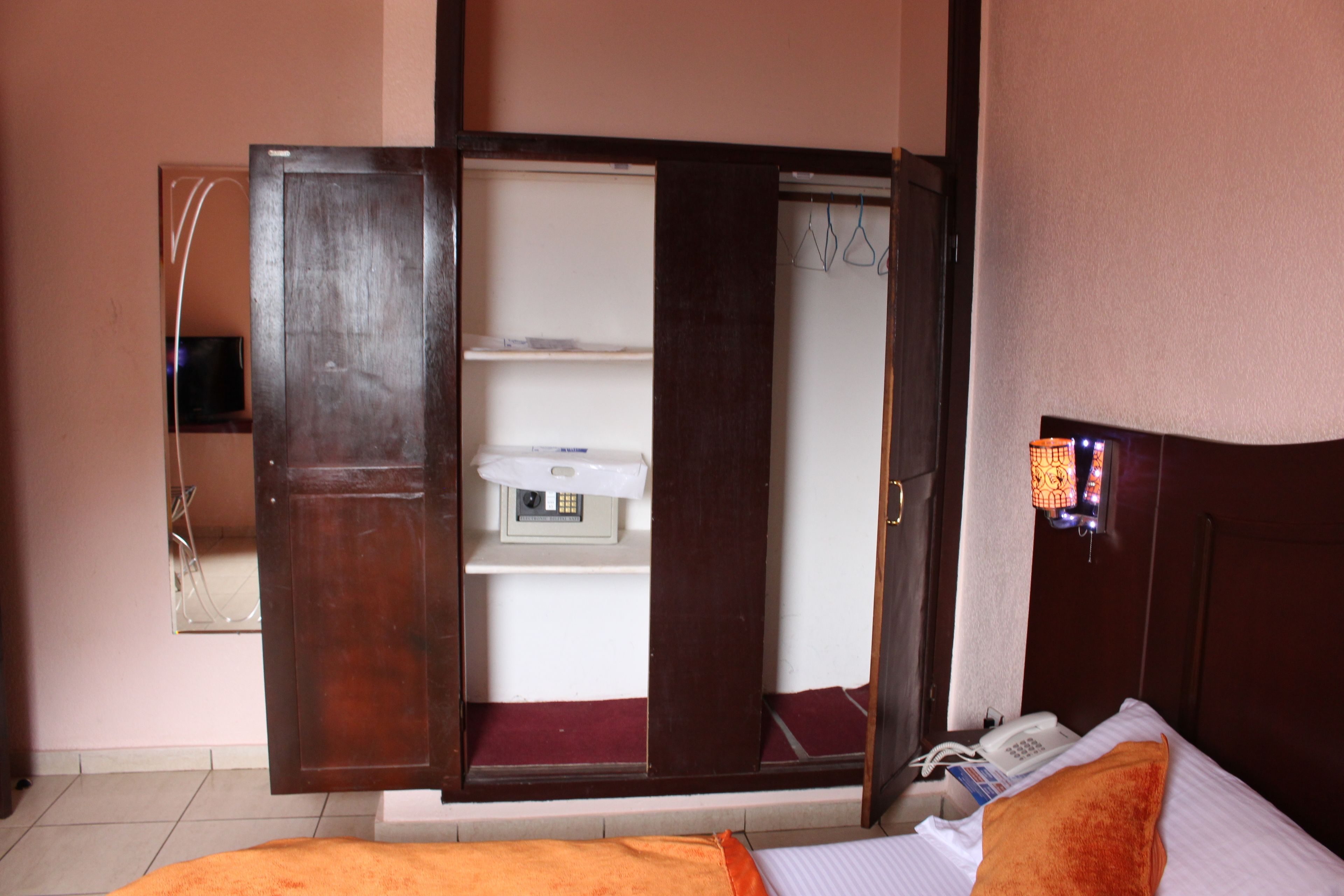 A hotel room with a bed, an open wardrobe, a bedside telephone, and a small shelf with a television.