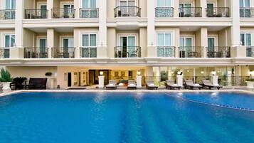 A hotel with a large indoor swimming pool, multiple balconies with metal railings, and a reception area with lounge chairs.