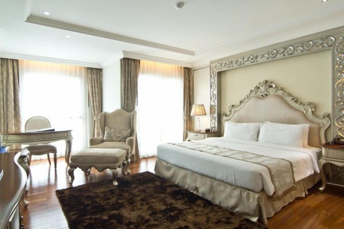 A hotel room with a large bed, a desk, a chair, and a window with curtains.