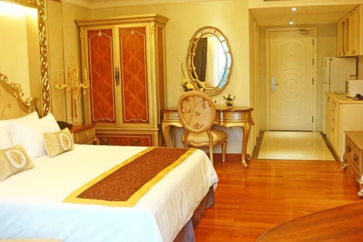 A hotel room with a bed, wardrobe, mirror, desk, and a door leading to the kitchen.