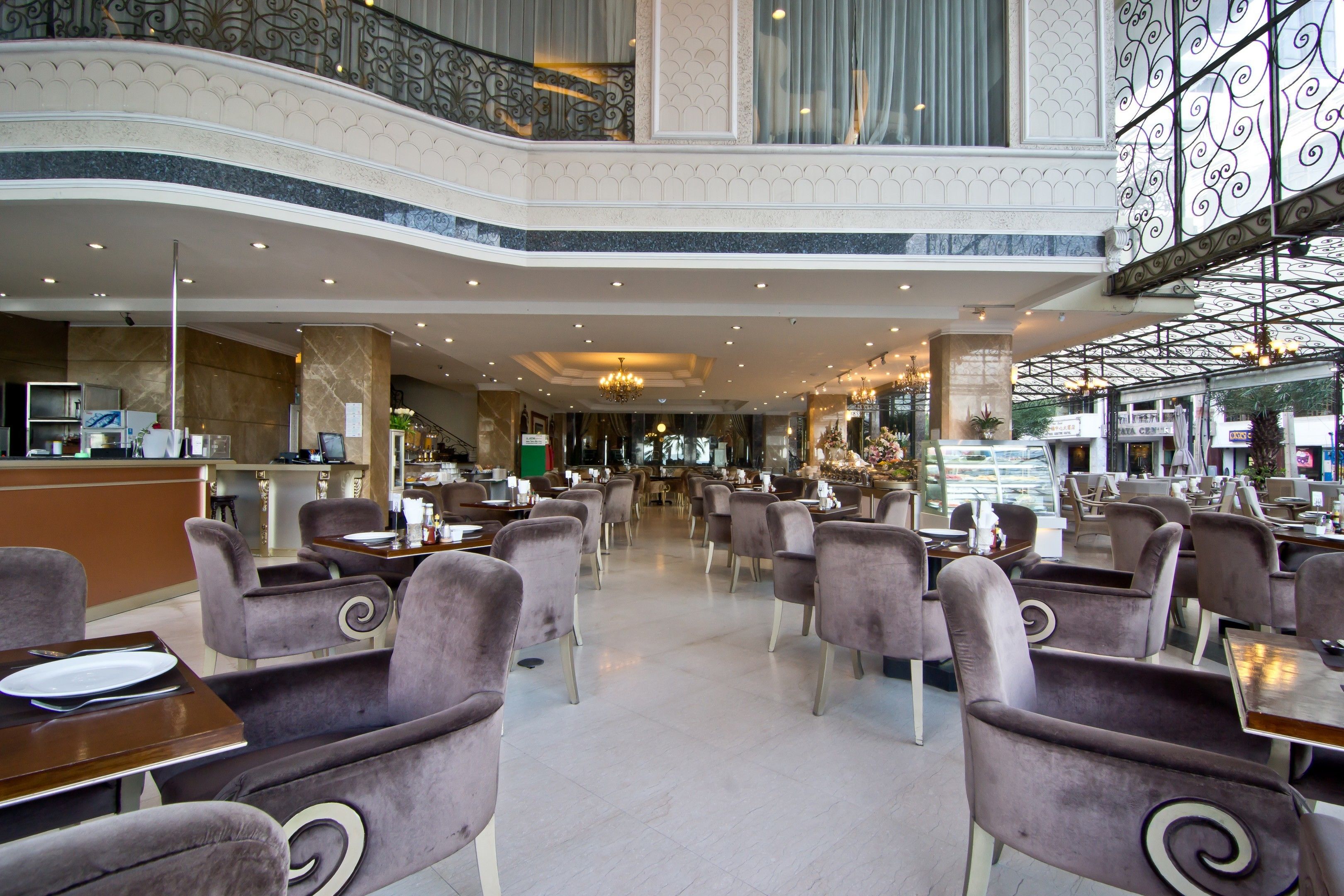 A spacious hotel lobby with multiple dining areas, a reception desk, and a decorative staircase.