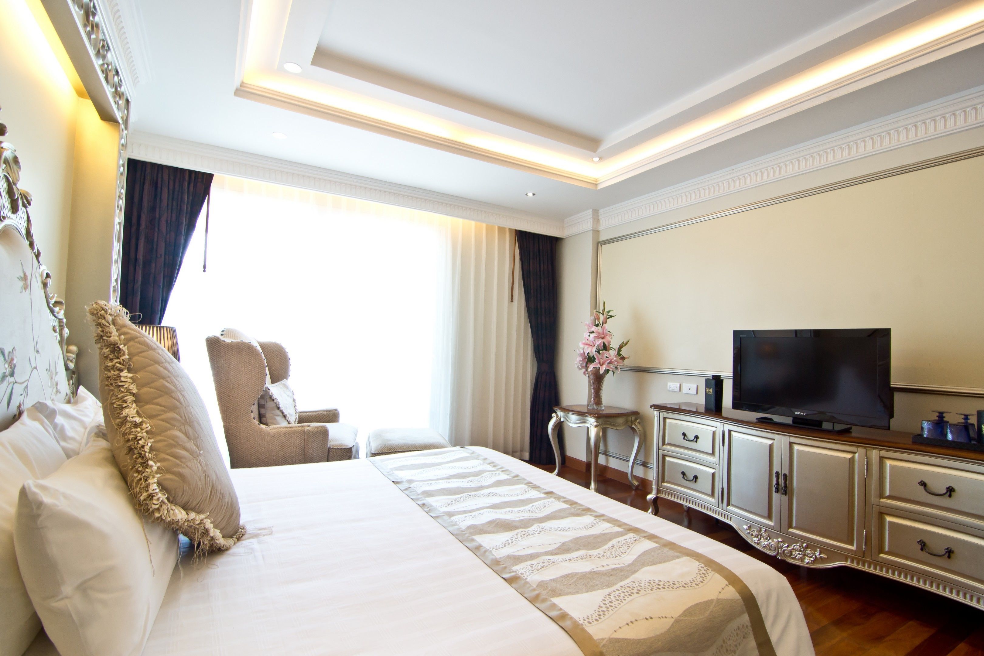 A hotel room with a large bed, a television, a side table, and a chair.