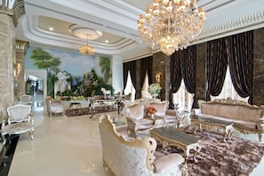 Eine luxuriöse Lobby mit aufwendigen Möbeln, einem prunkvollen Kronleuchter und einem Wandgemälde einer tropischen Landschaft.