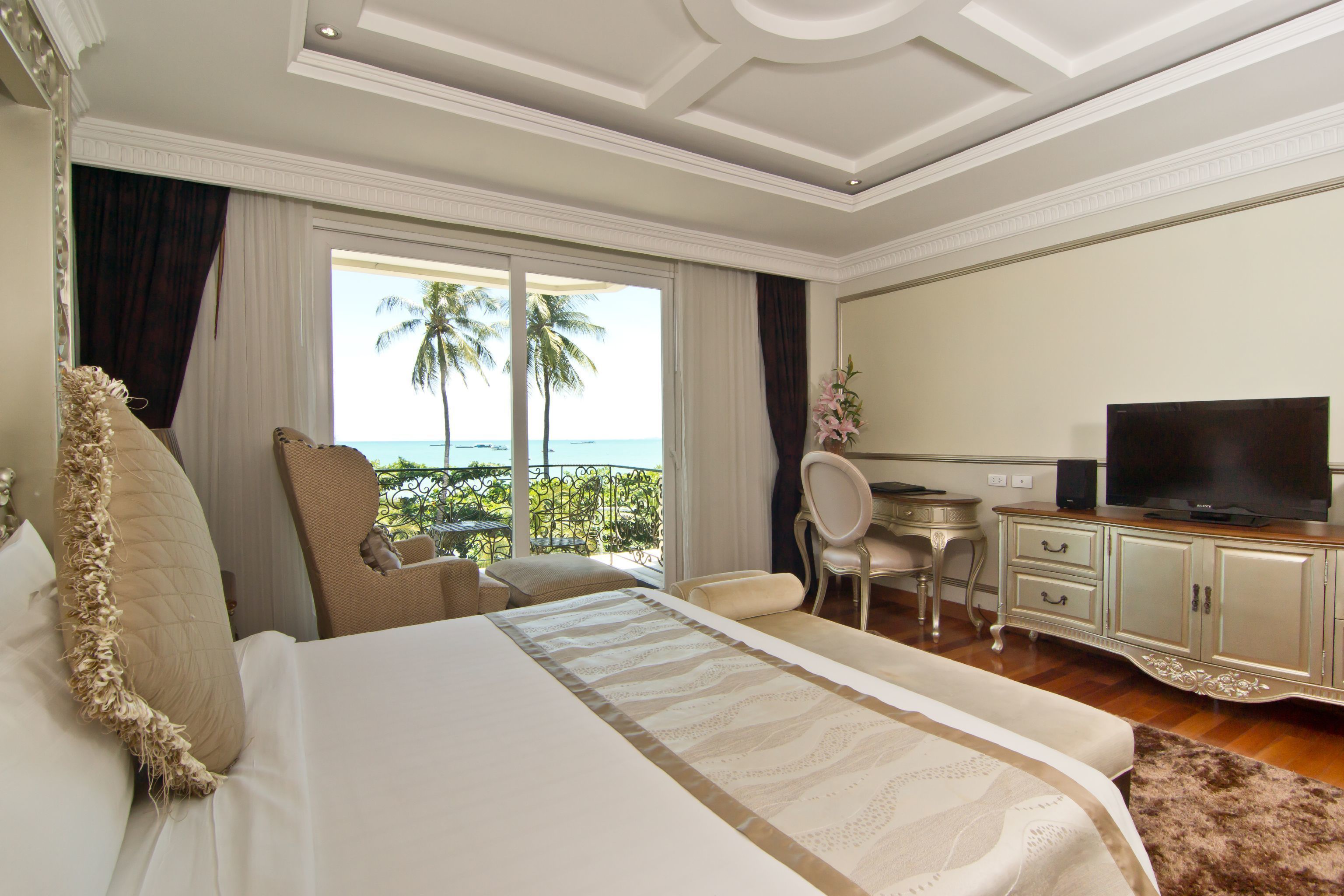 A hotel room with a bed, a desk, a television, and a view of the ocean.