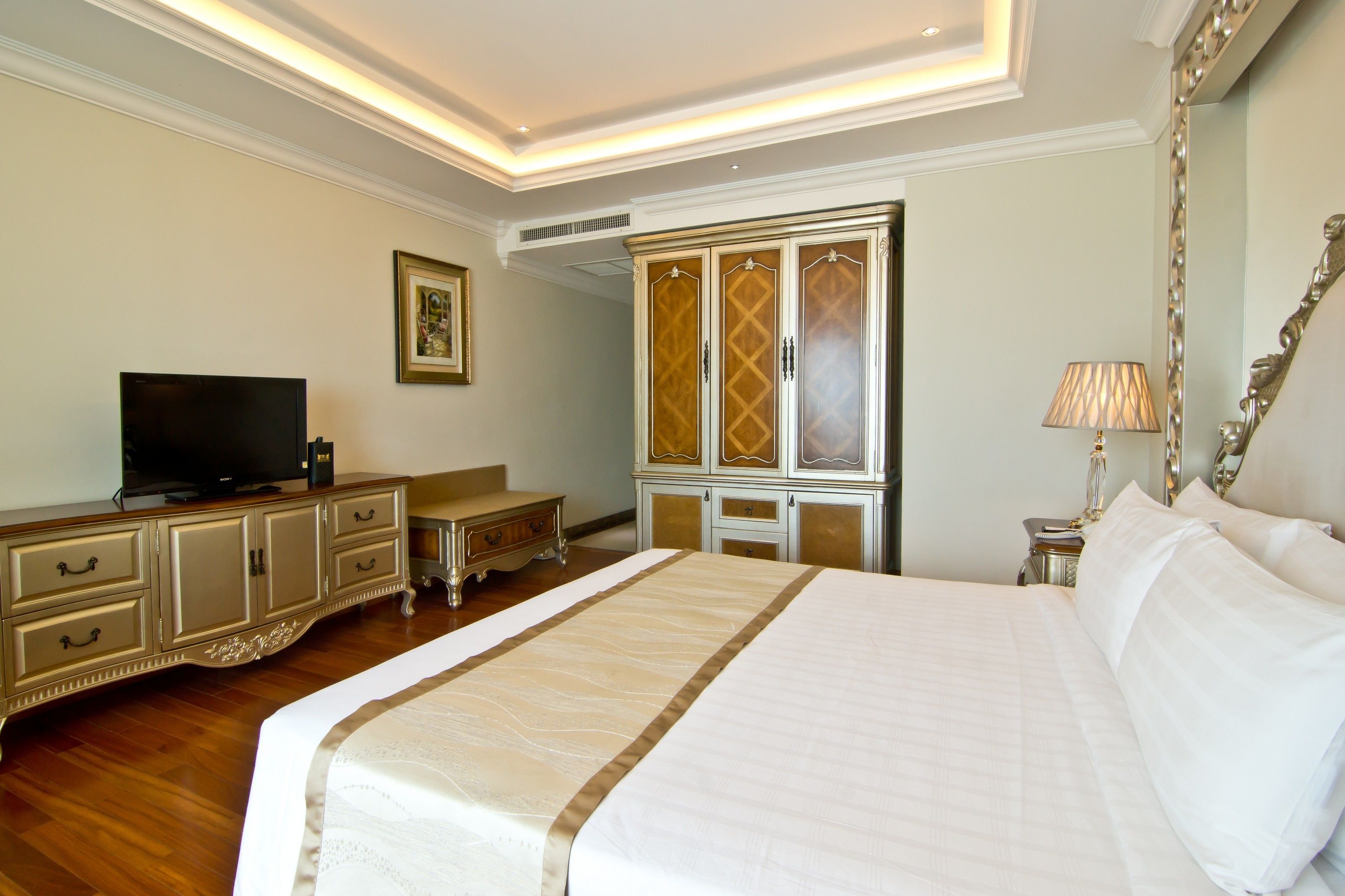 A hotel room with a large bed, a television on a dresser, a wardrobe, and a lamp.