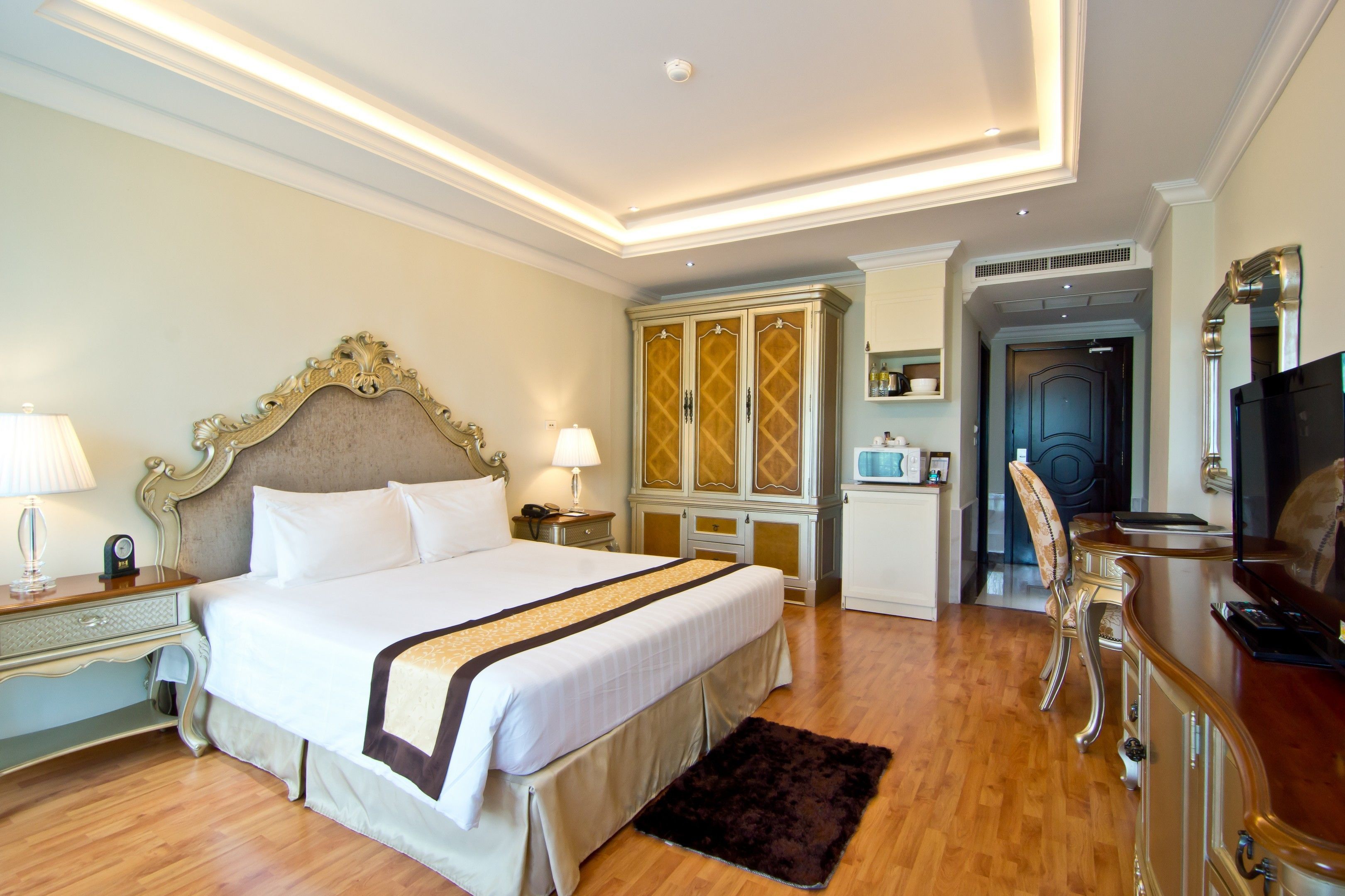 A hotel room with a large bed, a wooden floor, a TV, a desk, and a wardrobe.