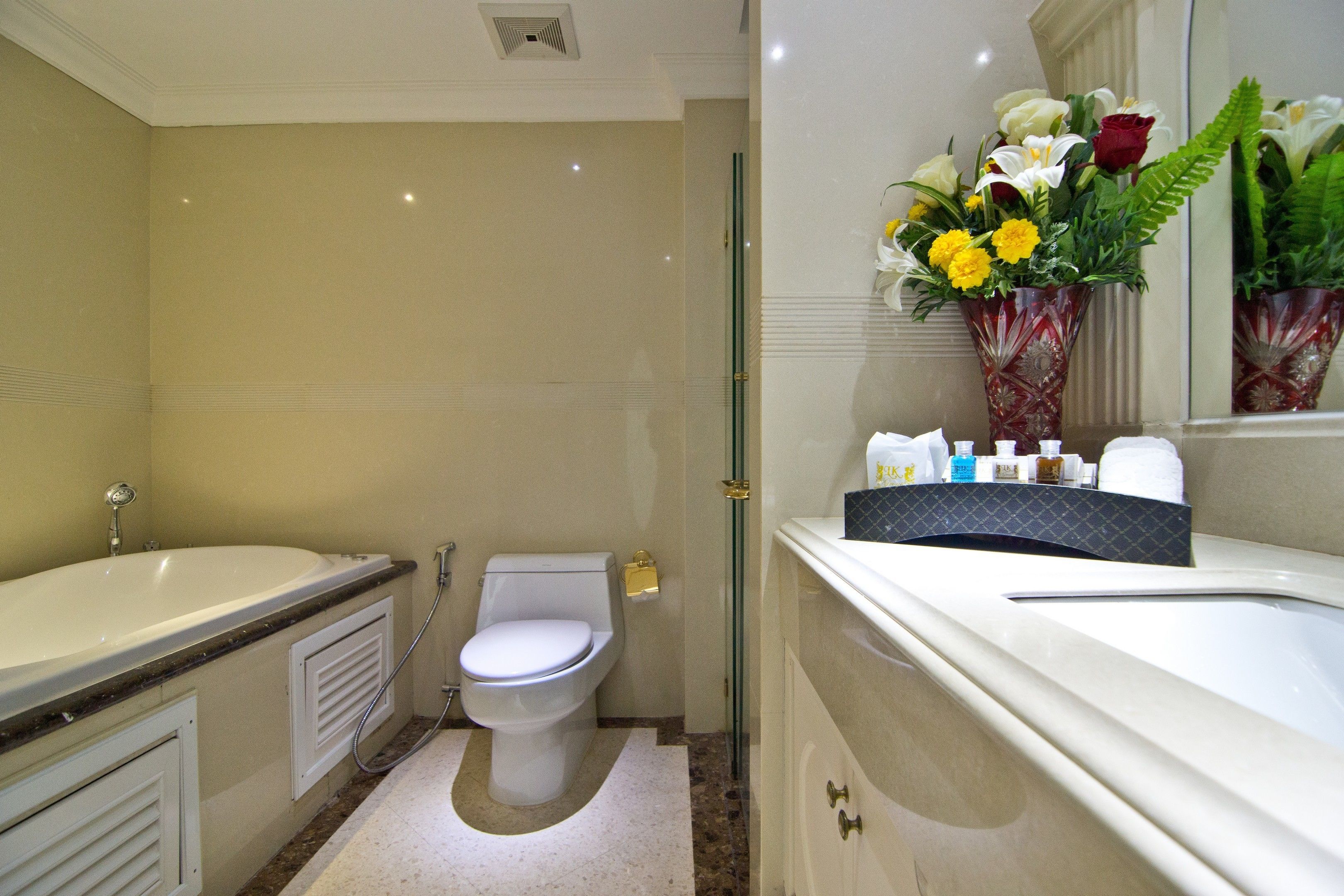 A bathroom with a bathtub, toilet, and shower. There is a vase with flowers on the vanity.