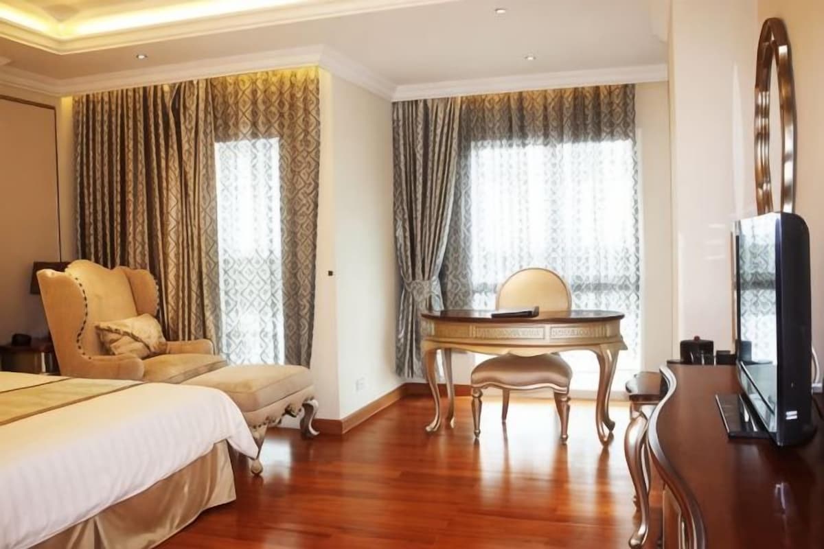 Habitación de hotel con cama, escritorio, silla, televisor y cortinas.