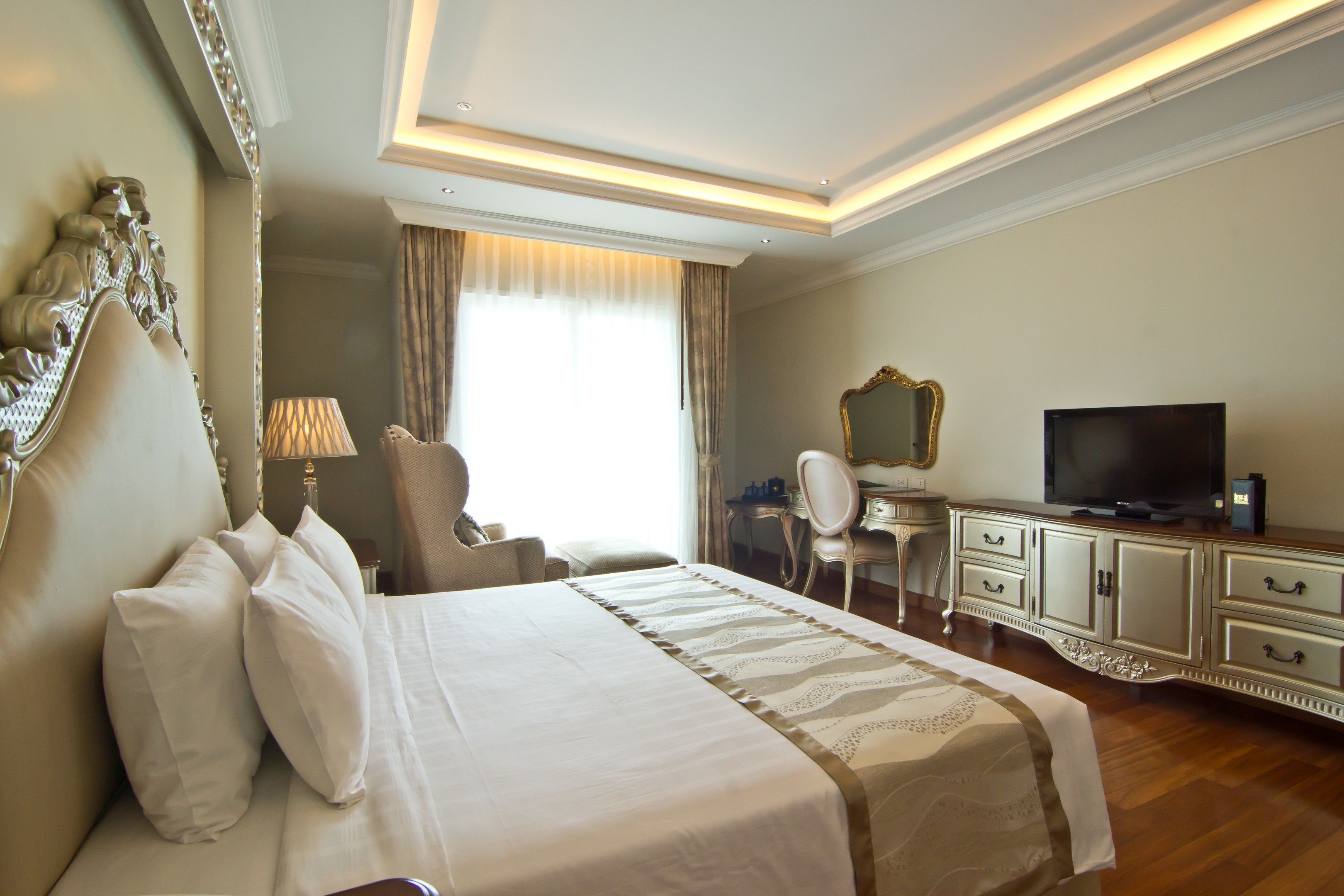 A hotel room with a large bed, a desk with a television, a chair, and a cabinet.