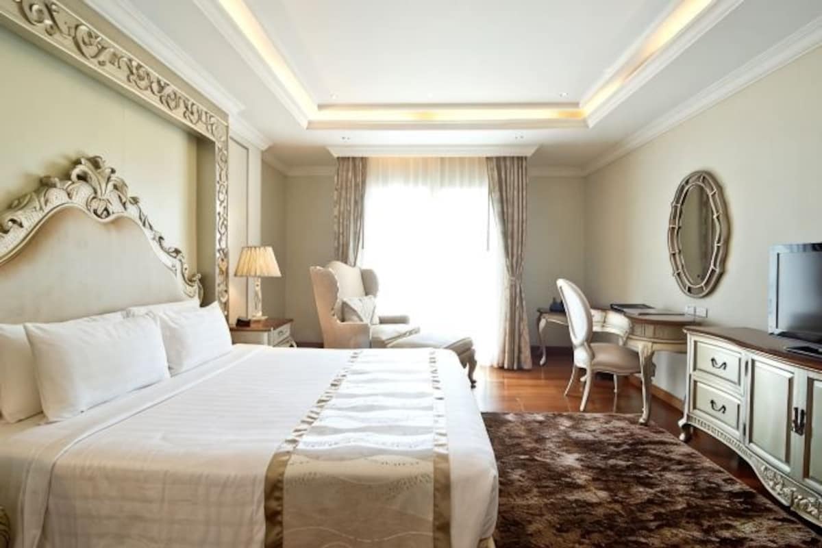 Habitación de hotel con una cama grande, un escritorio, una silla, un televisor y un espejo.