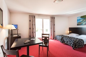 A hotel room with a desk, chair, two beds, a TV, and a painting on the wall.