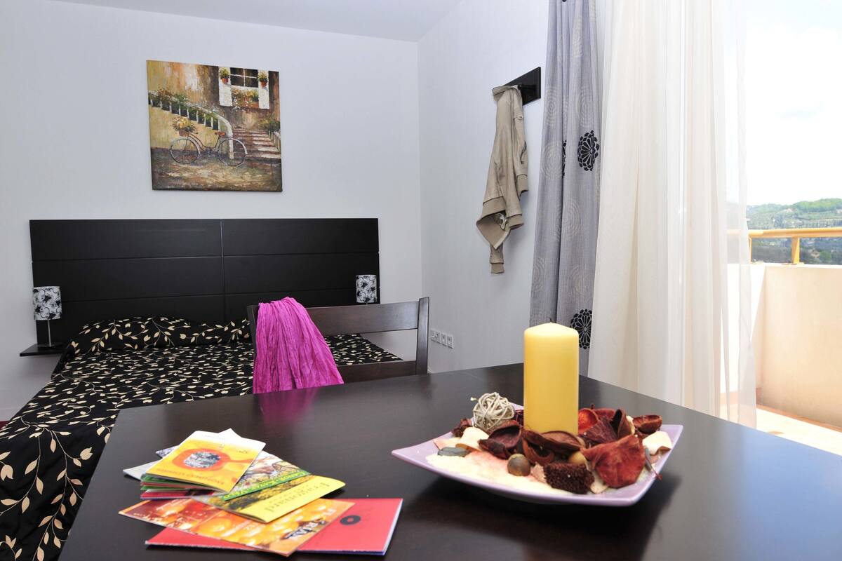 Une chambre d’hôtel avec un lit, une table sur laquelle se trouve une assiette de nourriture, une bougie et un tableau accroché au mur.