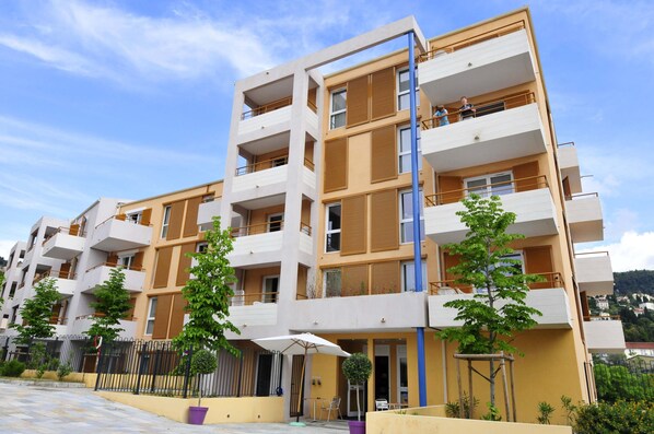 A multi-story residential building with balconies, a gated entrance, and outdoor seating areas.