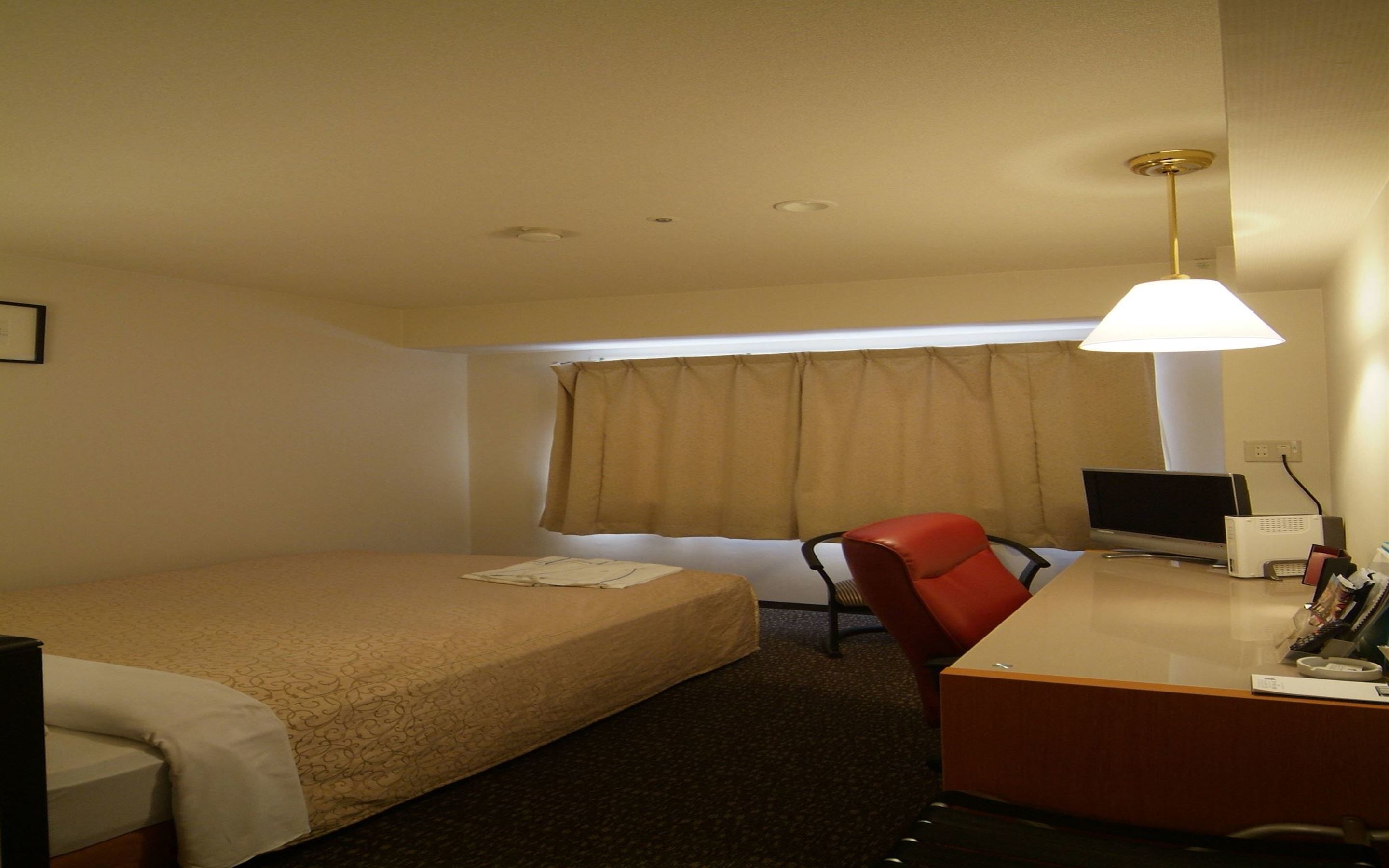 A hotel room with a single bed, a desk with a computer, a chair, and a window with curtains.