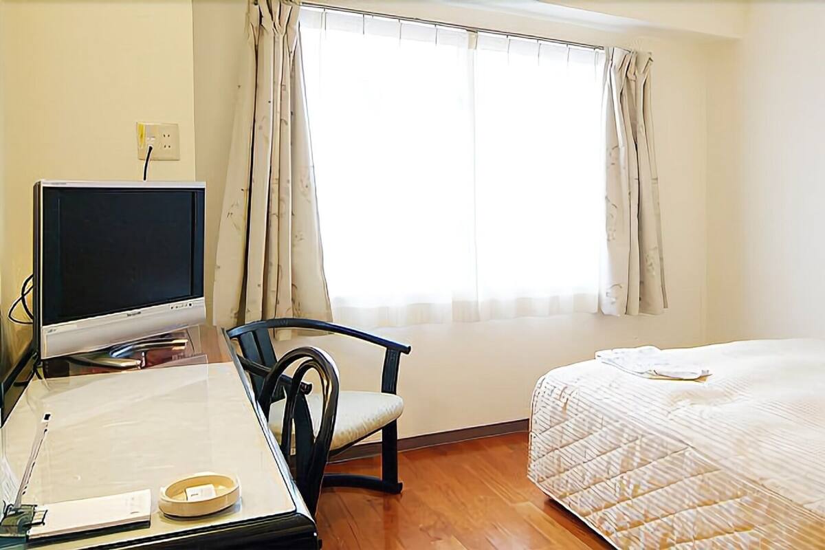 Una habitación pequeña y limpia con una cama, un escritorio con computadora y una silla.