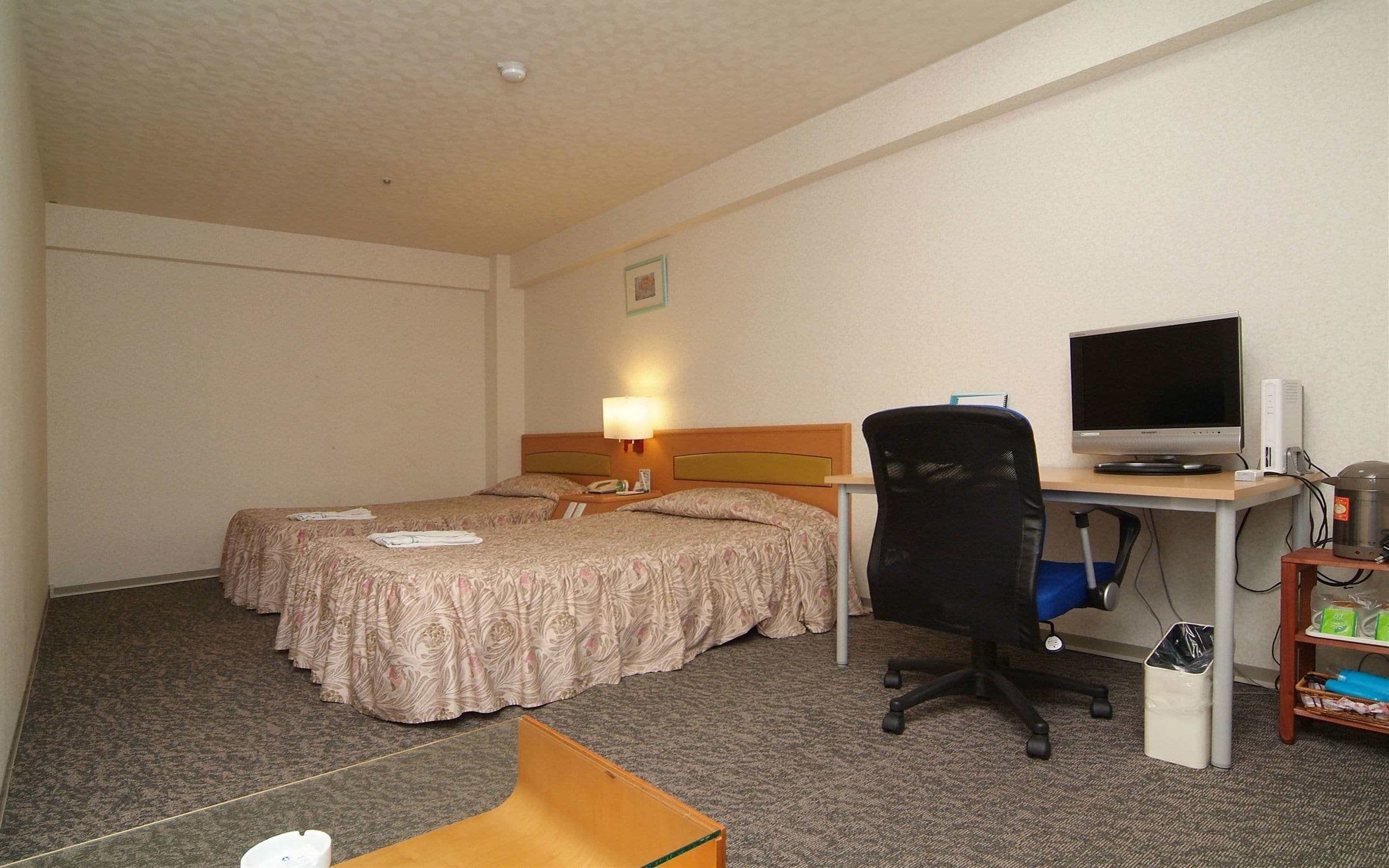 A hotel room with two beds, a desk with a computer, a chair, and a trash bin.