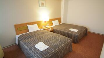 A hotel room with two beds, each with a patterned bedspread and pillows, a bedside table with a lamp, and a framed picture on the wall.