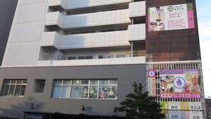 A multi-story building with a modern architectural design, featuring a series of balconies and a ground-level entrance with a covered area. - Hotel Crown Hills Himeji (Himeji)