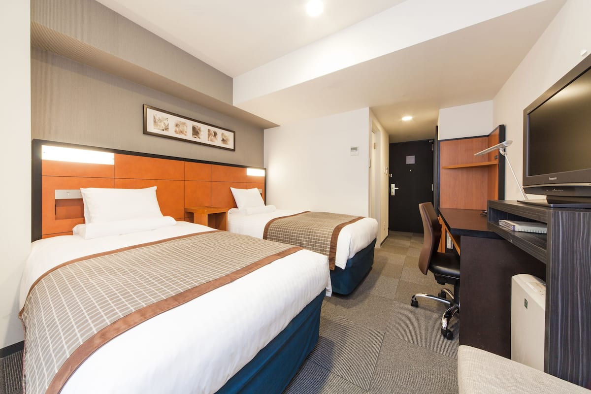 Une chambre d’hôtel avec deux lits, un bureau, une chaise, une télévision et un tableau encadré au mur.