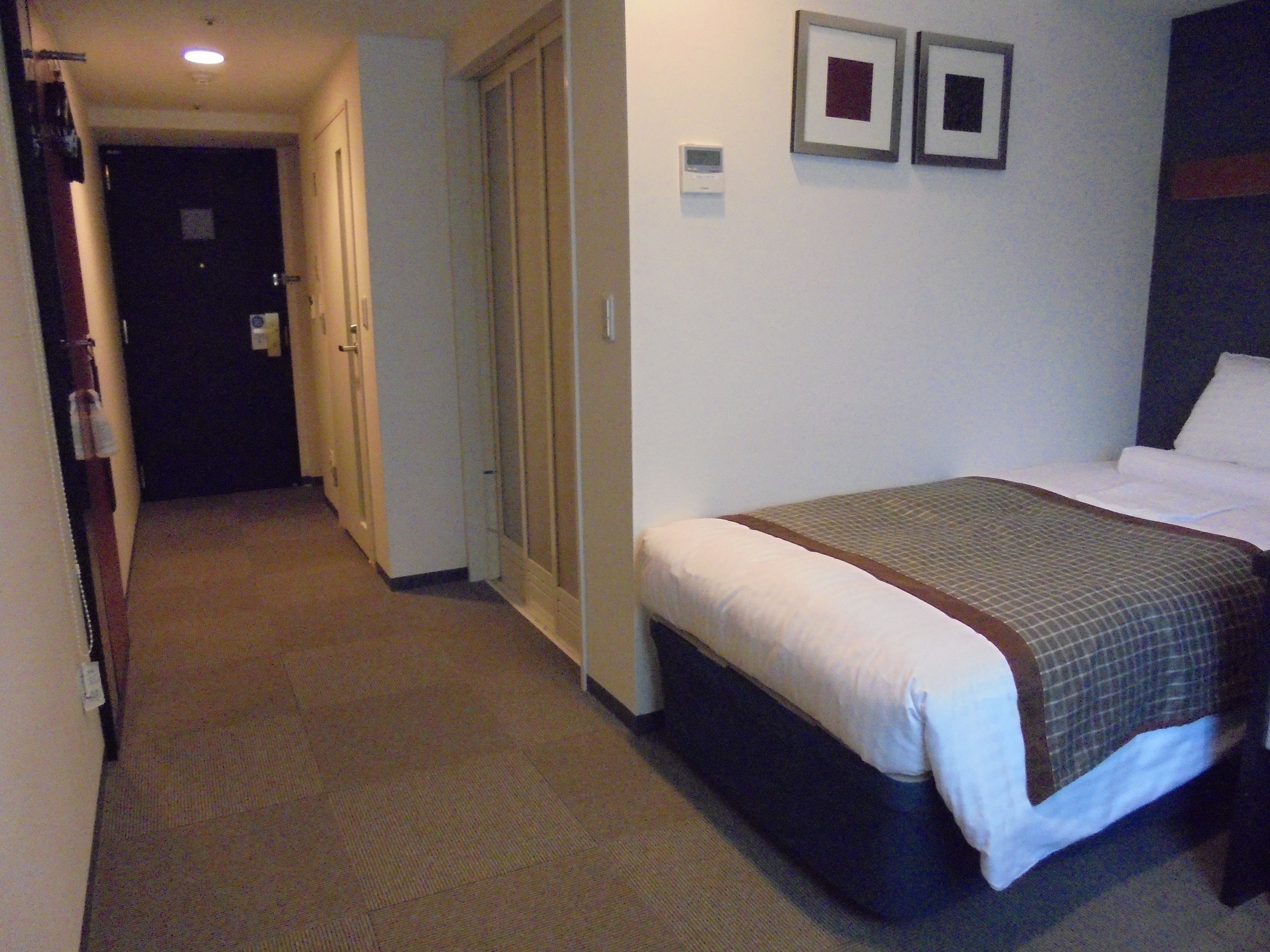 Habitación de hotel con cama, puerta y termostato fijado a la pared.
