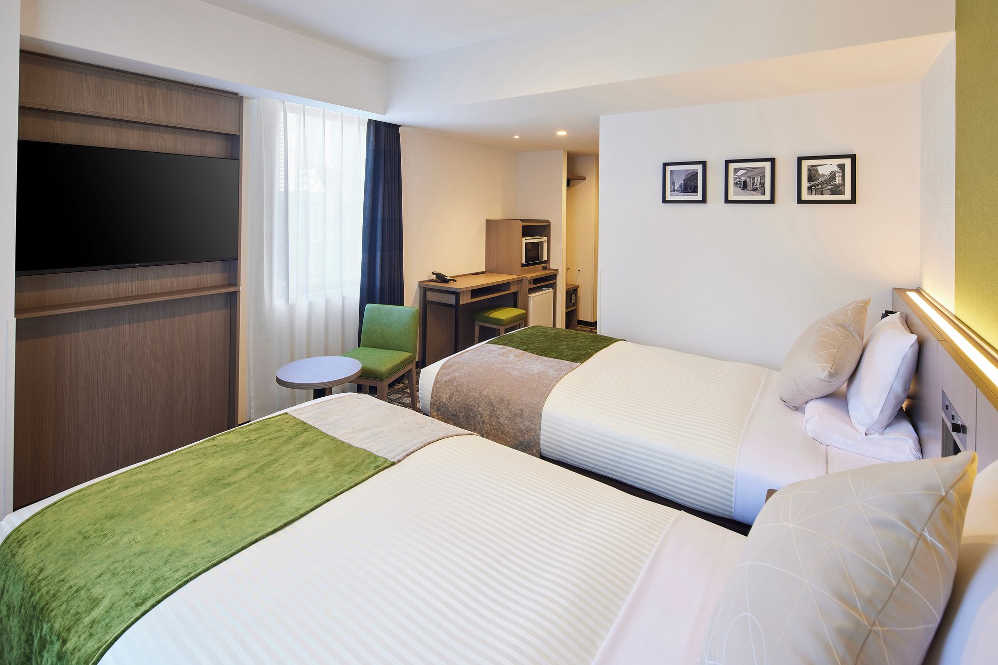 Ein Hotelzimmer mit zwei Betten, einem Schreibtisch, einem Sessel und einem Fernseher.
