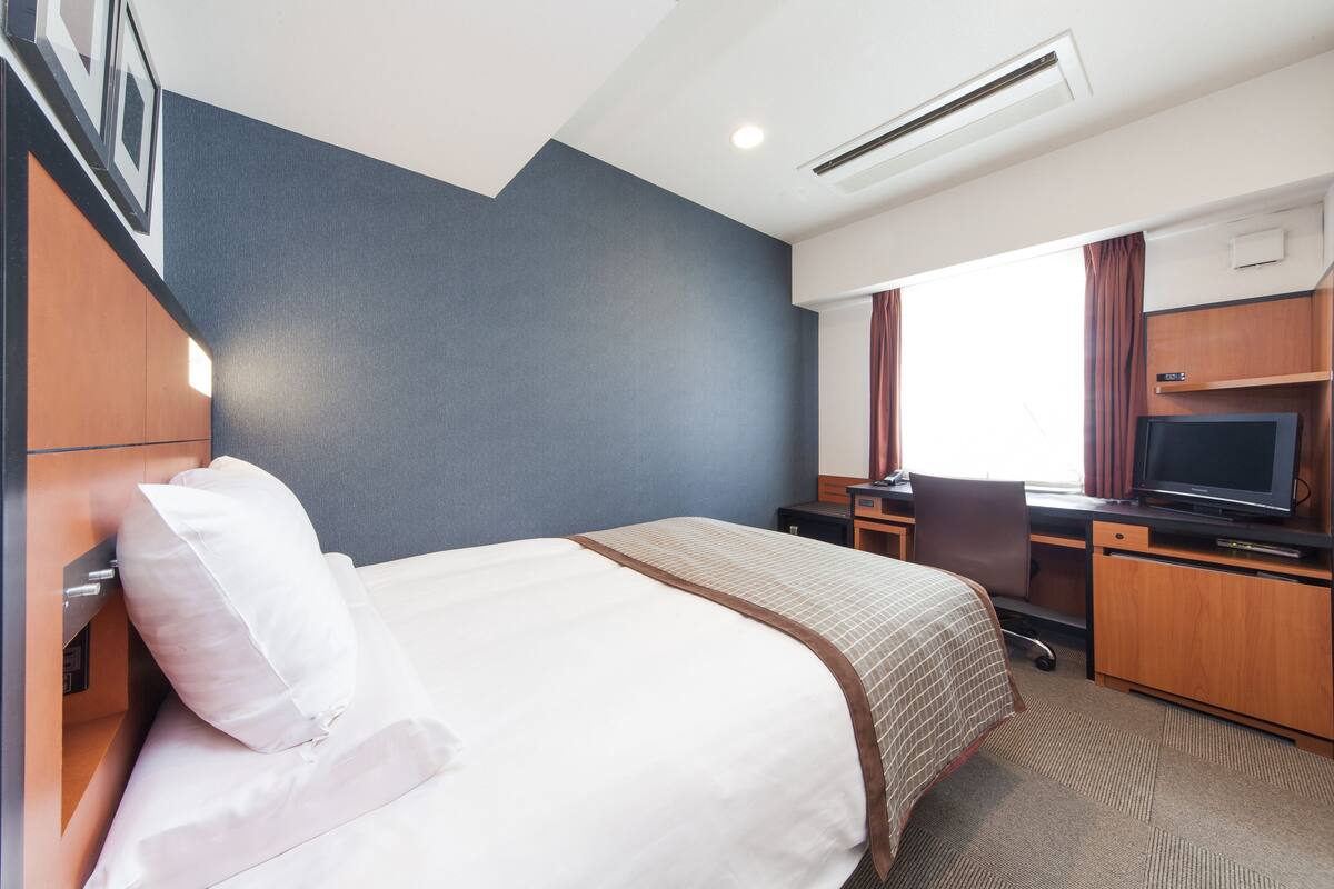 Une chambre d’hôtel équipée d’un lit, d’un bureau, d’une chaise, d’une télévision et d’une fenêtre avec des rideaux.