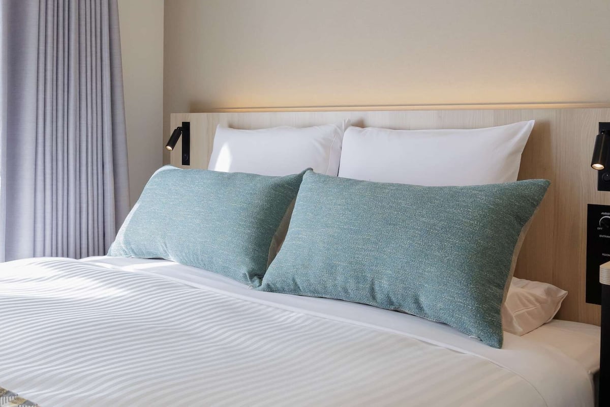 Une chambre d’hôtel avec un lit, une tête de lit, une table de chevet et une lampe.