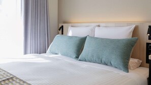 Ein Hotelzimmer mit Bett, Kopfstütze, Nachttisch und Lampe.